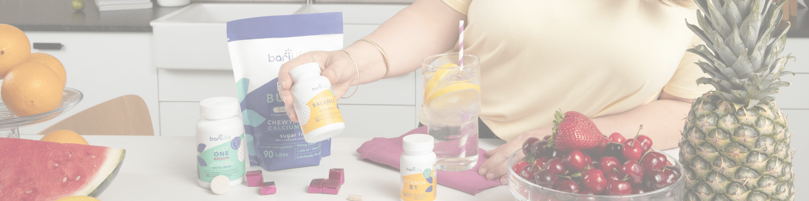 Person holding a bottle of vitamins with fresh fruits in a bright kitchen setting.